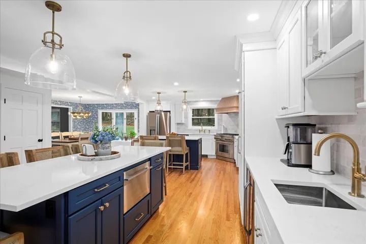 Spacious, modern kitchen with navy island, white countertops, copper range hood, and wood floors.