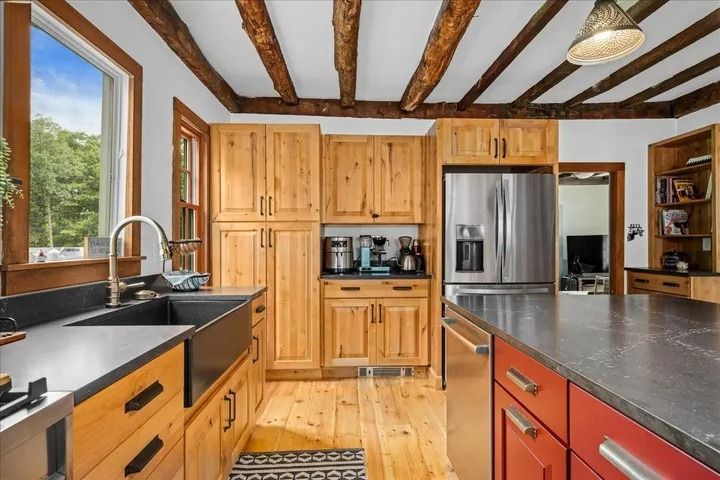 Rustic kitchen with light wood cabinets, dark countertops, and exposed beams.