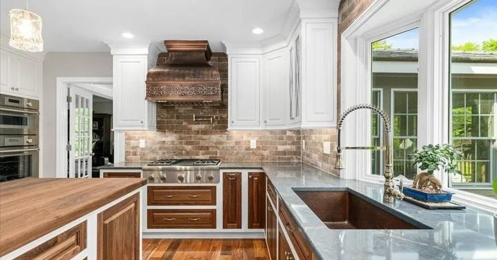 Elegant kitchen with white cabinets, copper range hood, and large window overlooking a yard.