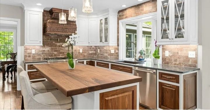 Kitchen with white cabinets, wood island, brick backsplash, and a window.