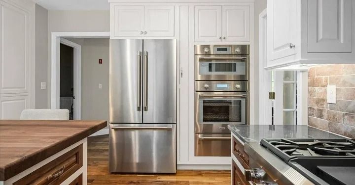 Stainless steel appliances in a bright kitchen with white cabinets, and wooden accents.