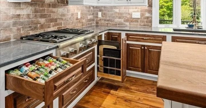 Kitchen cabinet with pull-out spice rack and drawer, dark wood cabinets, stove, and light wood floor.