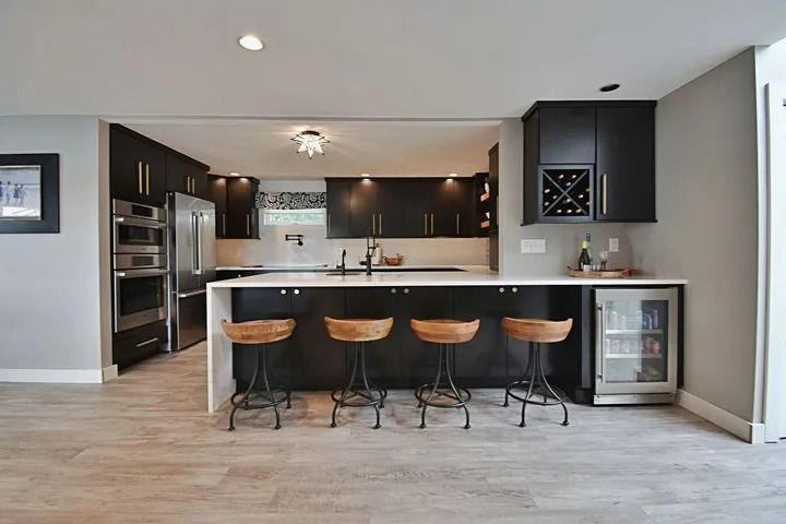 Modern kitchen with dark cabinets, a white countertop, and bar stools. Includes built-in appliances and a small refrigerator.