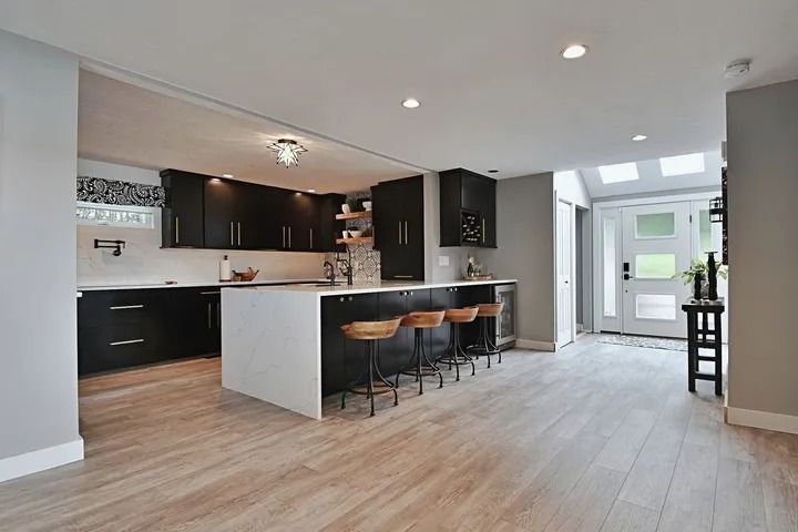 Modern kitchen with black cabinets, white countertops, and wood flooring, with a breakfast bar.