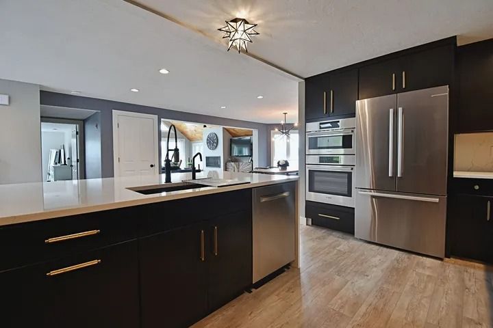 Modern kitchen with black cabinetry, stainless steel appliances, and a white countertop island.