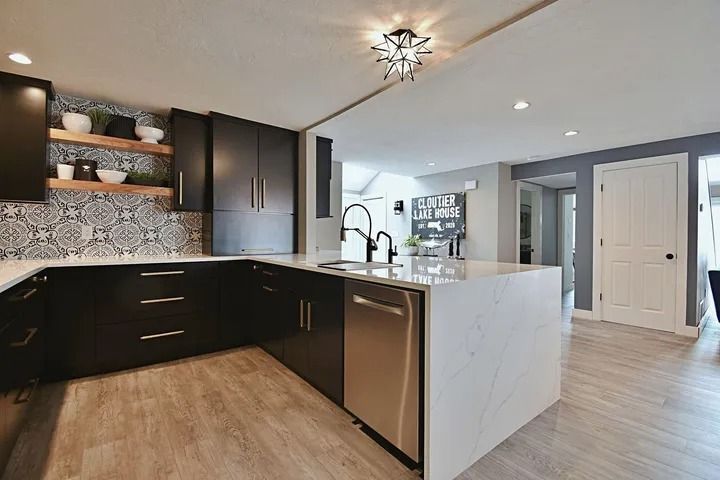 Modern kitchen with black cabinets, white countertops, and stainless steel appliances.