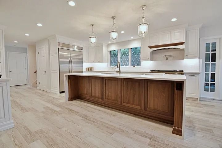 Modern kitchen with white cabinets, wood island, stainless steel fridge, and light wood flooring.