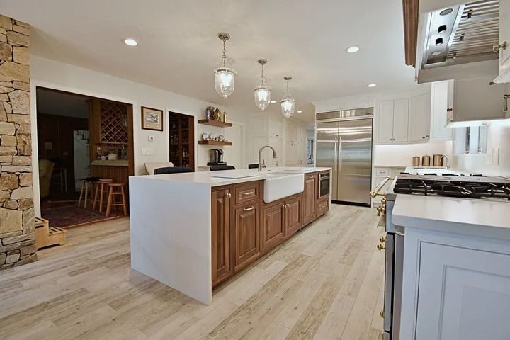 Spacious kitchen with a large island, stainless steel appliances, and wood cabinetry, lit by hanging pendant lights.