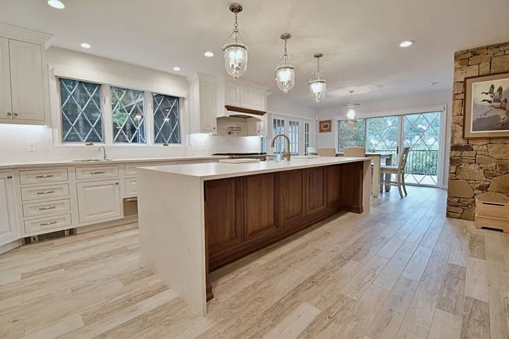 Spacious white kitchen with dark wood island, pendant lights, and large windows.