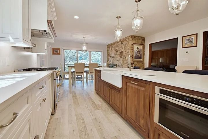 Spacious kitchen with a large island, white countertops, and wooden cabinetry. A stone wall is visible.