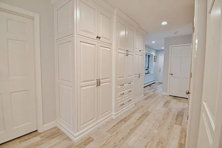 White cabinets line a hallway with light wood flooring. Two doors are on either side.