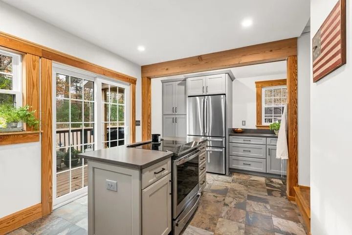 Kitchen with island, stainless steel appliances, gray cabinets, wooden trim, and sliding glass door.