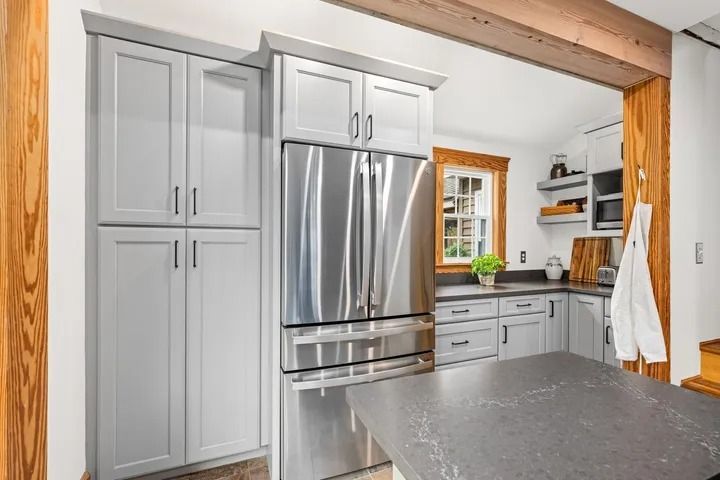 Grey kitchen with stainless steel refrigerator, cabinets, and island; rustic wood trim.