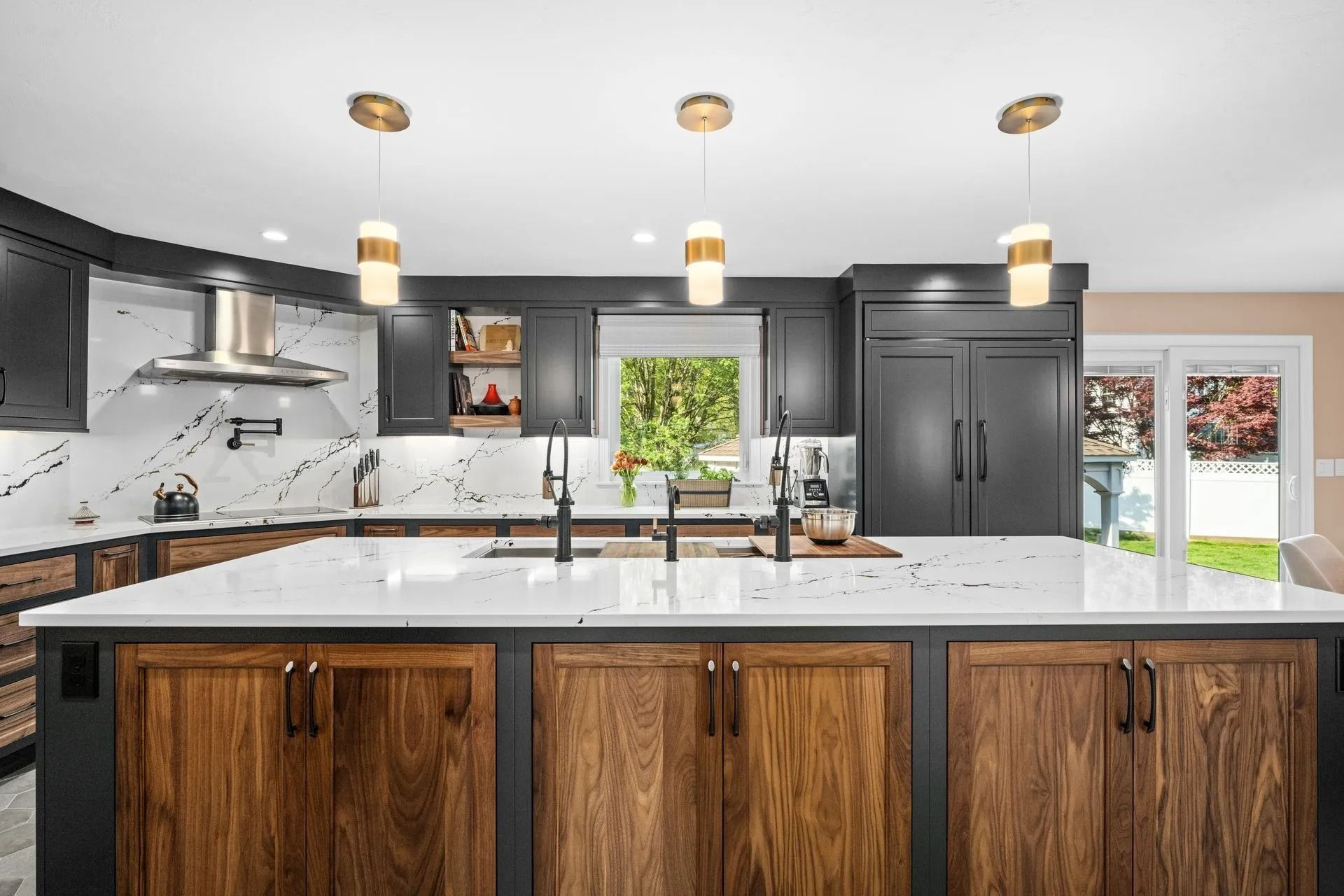 Modern kitchen with dark cabinetry, wood island, white countertops, and gold pendant lights.