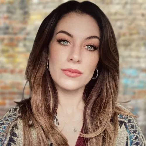 Woman with long, ombre brown hair, hoop earrings, and neutral makeup, looking at the camera.