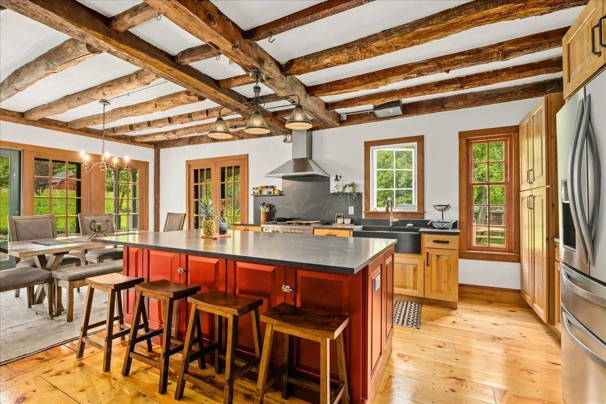Open-concept kitchen with red island, wooden beams, dining area, and stainless steel appliances.