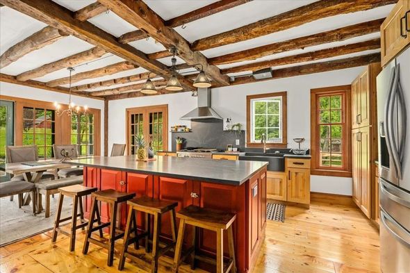Kitchen with exposed wooden beams, red island with stools, and stainless steel appliances.