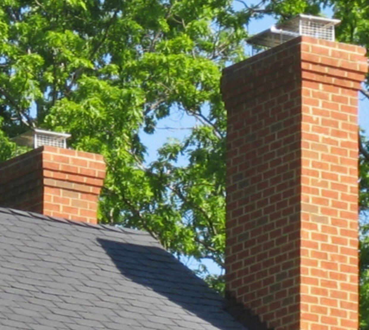 A brick chimney on top of a roof with trees in the background.