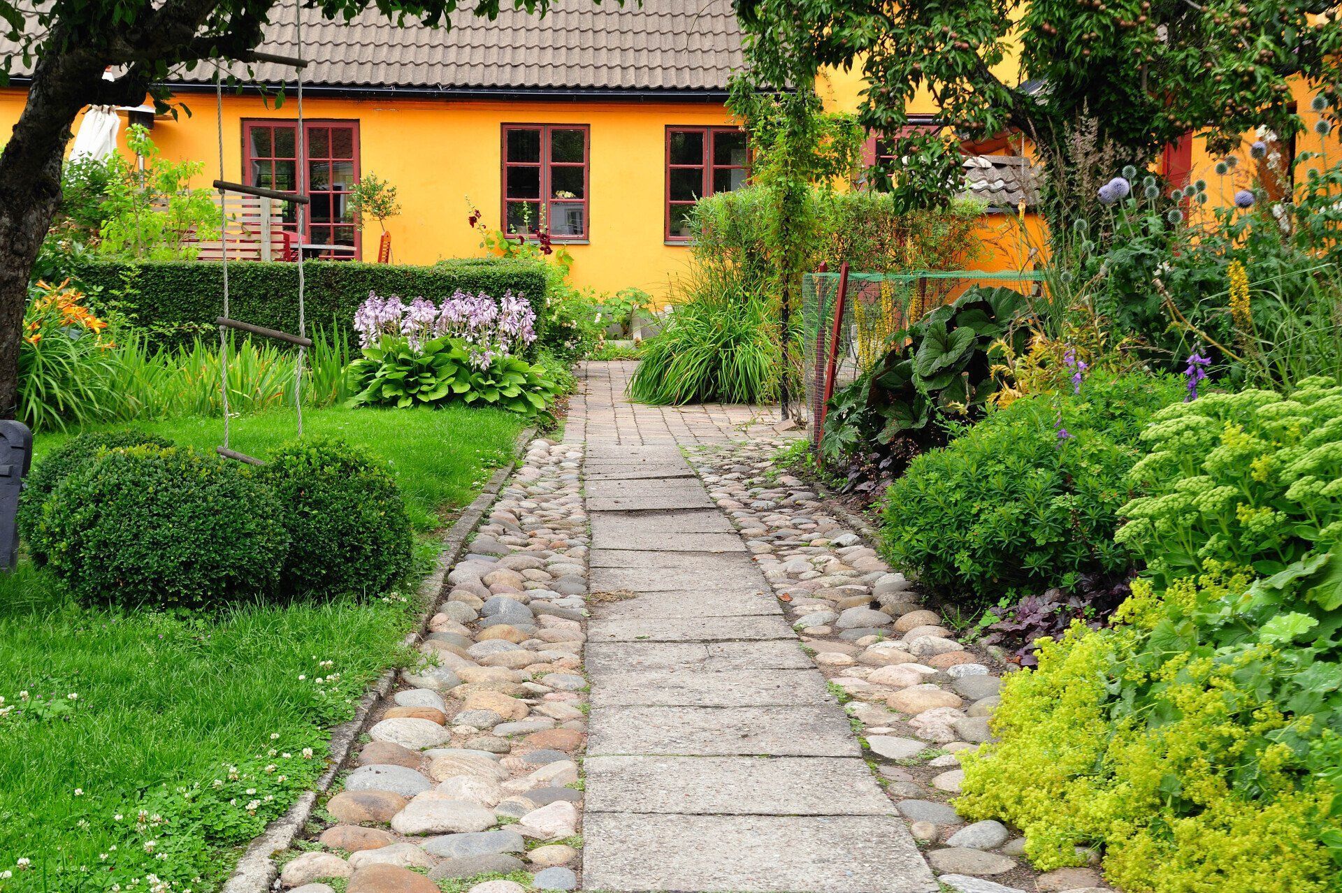 A stone path leading to a yellow house in a garden.