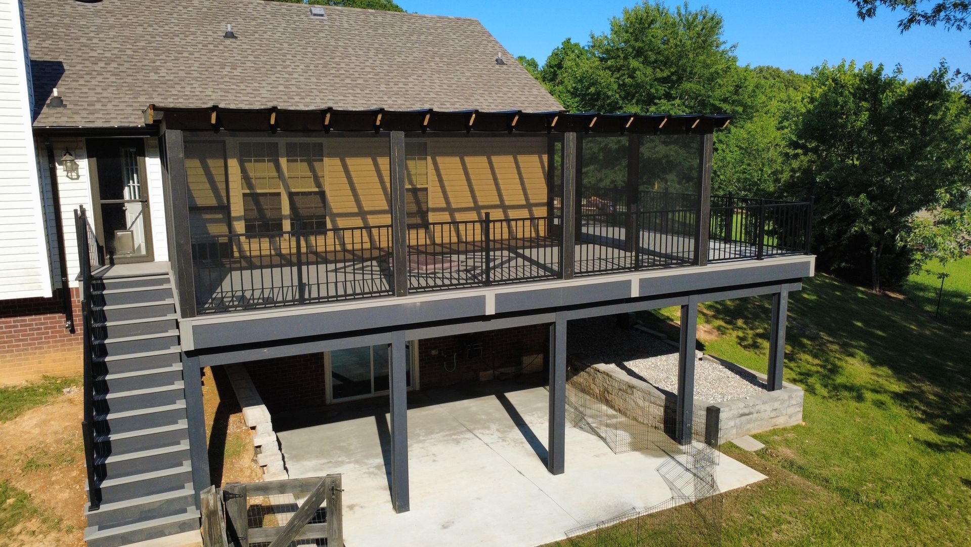 Backyard deck with black railing, steps, and screened porch beneath a house