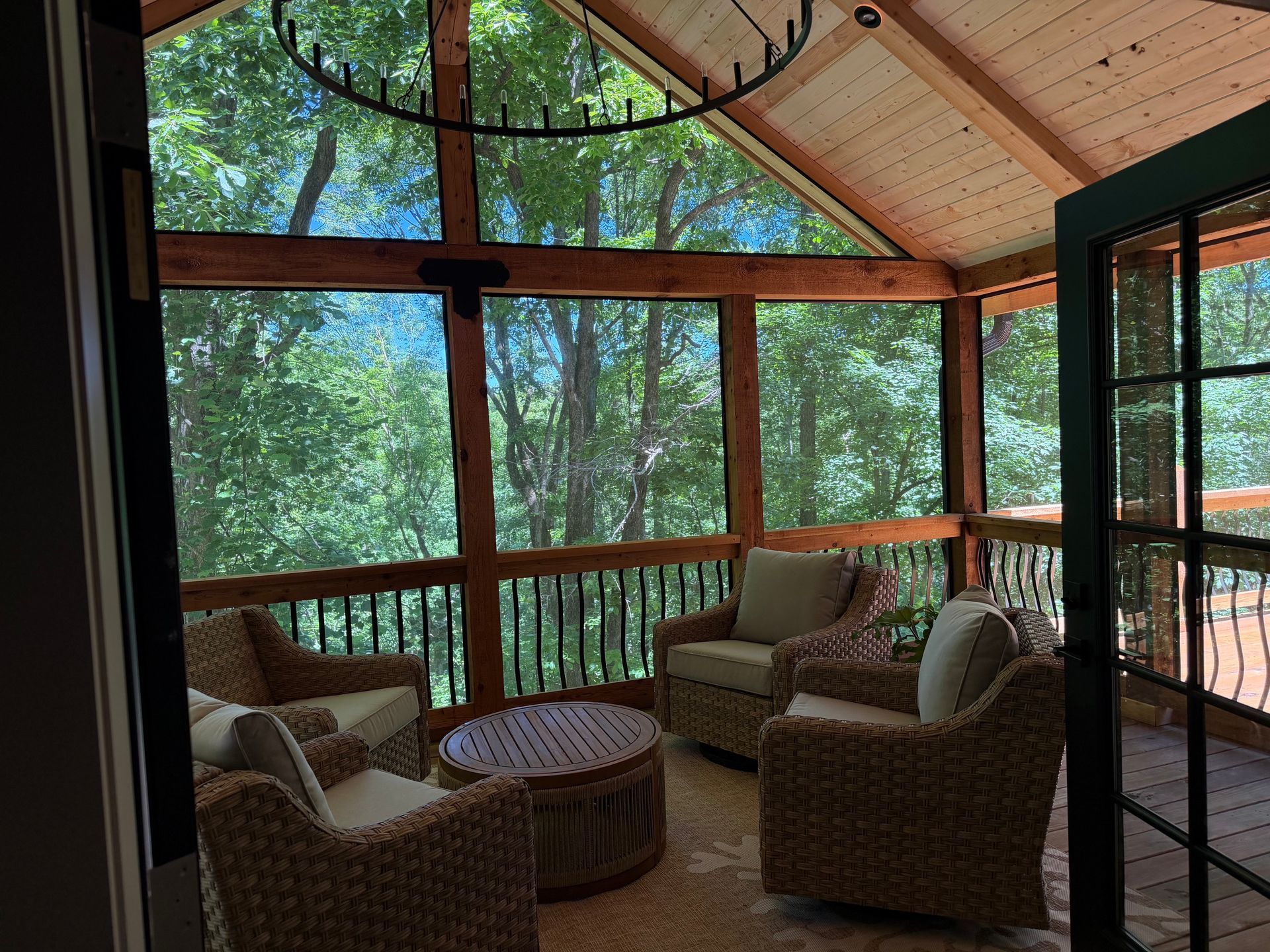 Sunroom with wicker chairs, round table, and large windows overlooking a wooded view