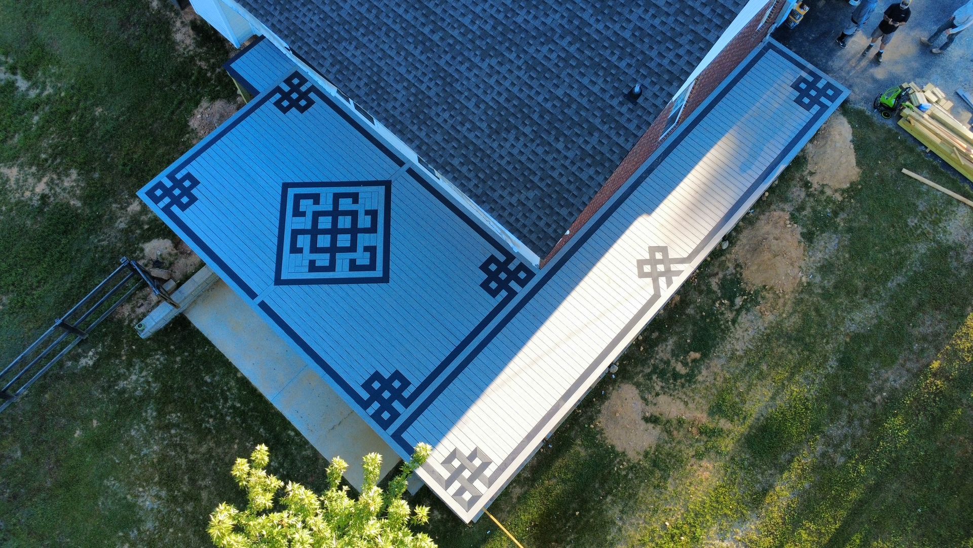 Aerial view of a blue-roofed building with dark geometric patterns beside a grassy area.