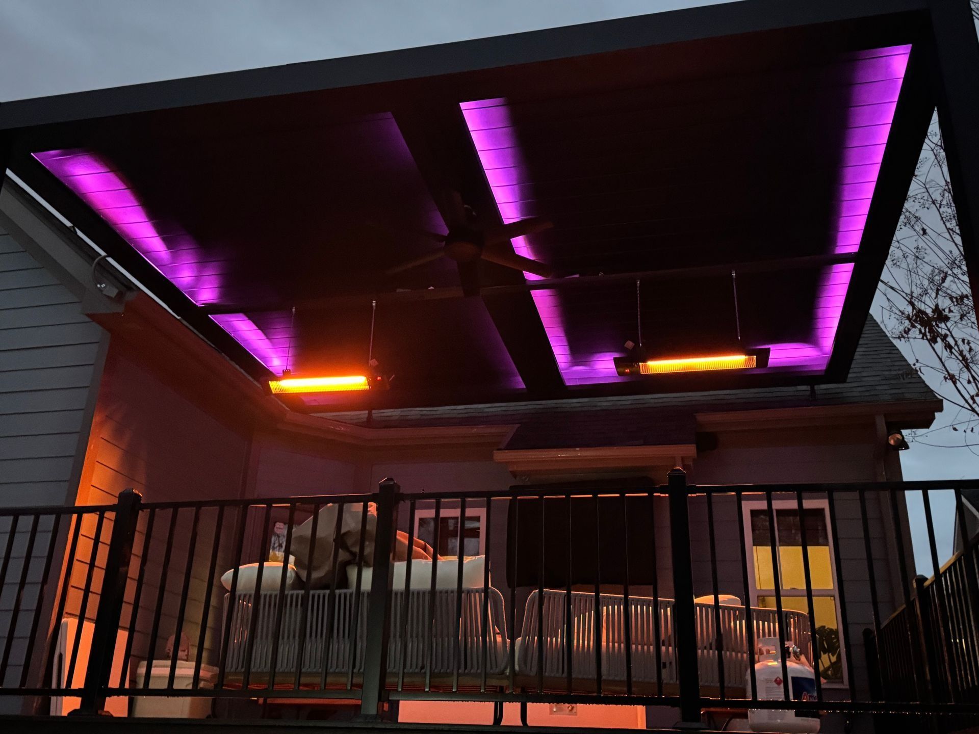 Covered patio with purple LED strip lights and a black railing at dusk