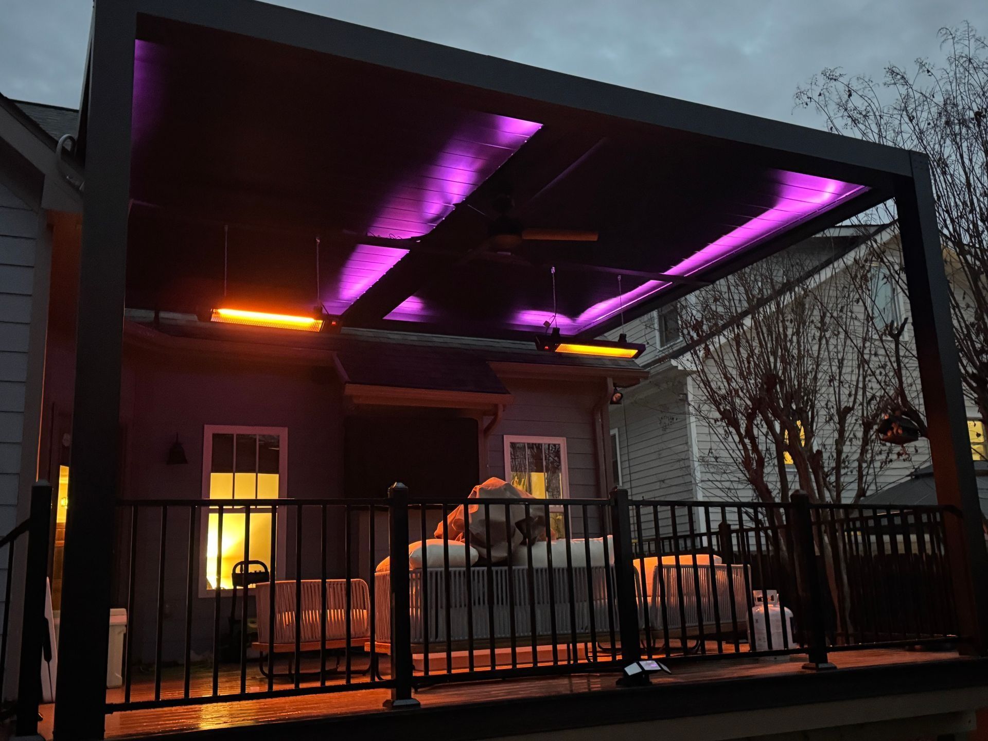 Carport with purple and orange lights, a parked car, and a couch behind a black fence at dusk