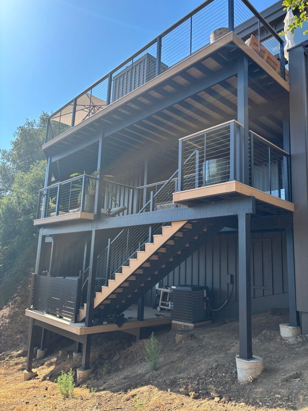 Two-story deck with metal stairs and railing on a raised house exterior in a wooded area