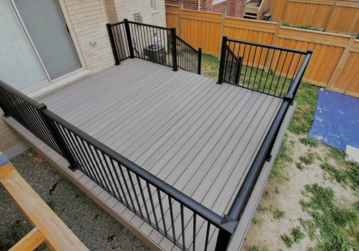A composite deck with black railing and steps, in a backyard setting.