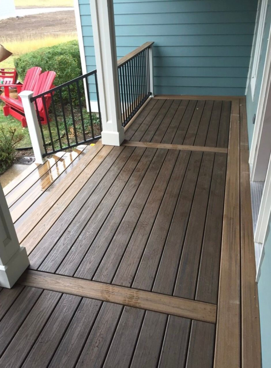 Wooden porch with brown decking and light wood trim, black railing. Blue siding in background.