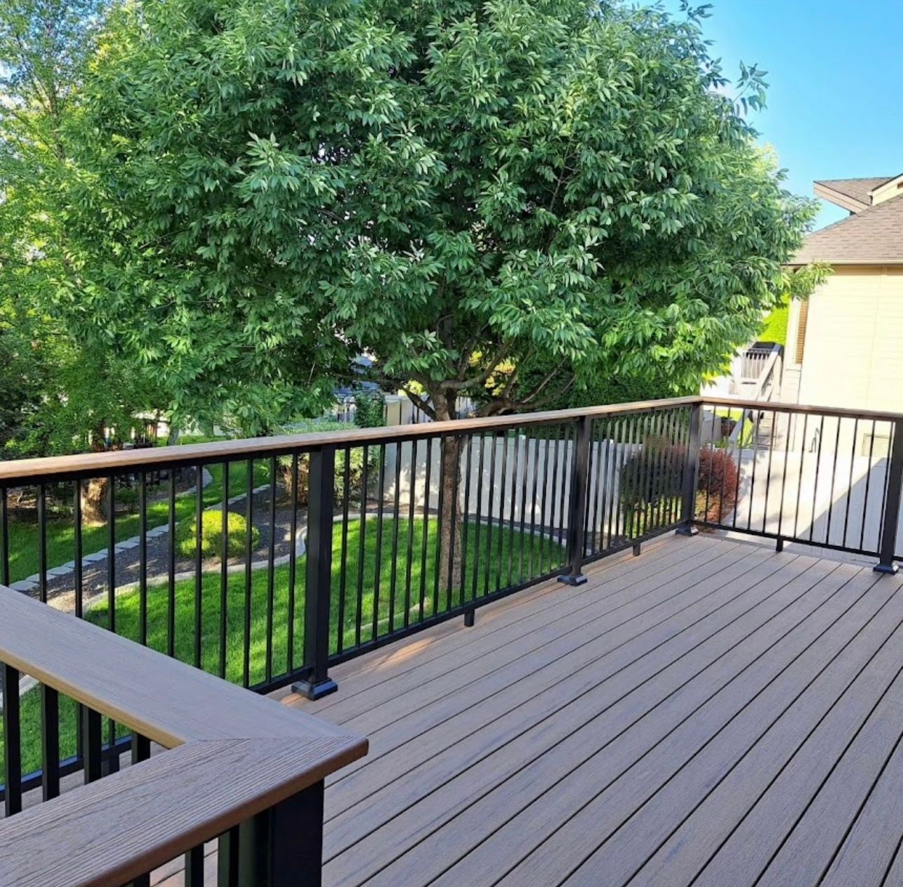 Wooden deck with black railings overlooking a backyard with a large tree.