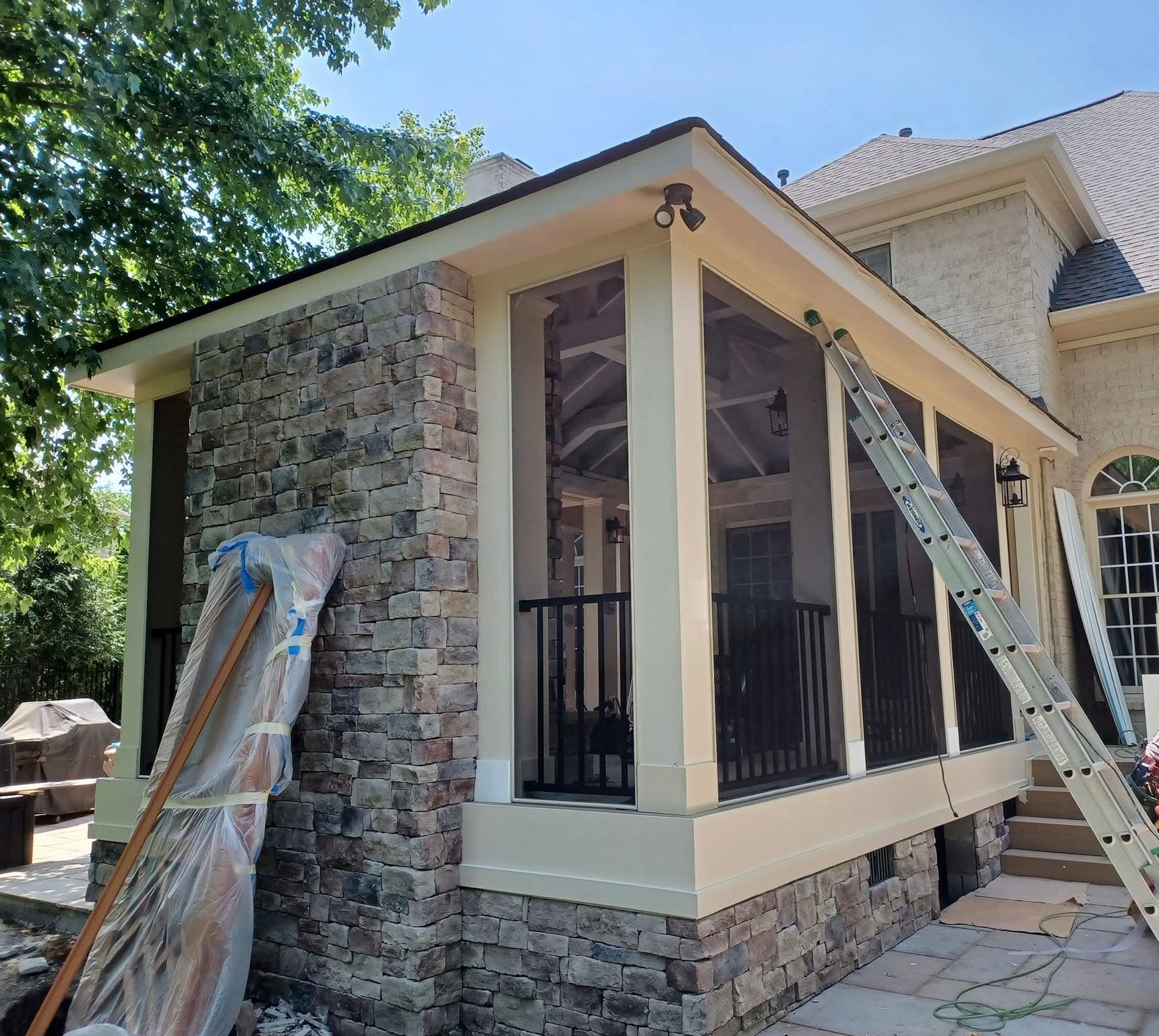 Stone and screened porch extension on a house; ladder propped up.
