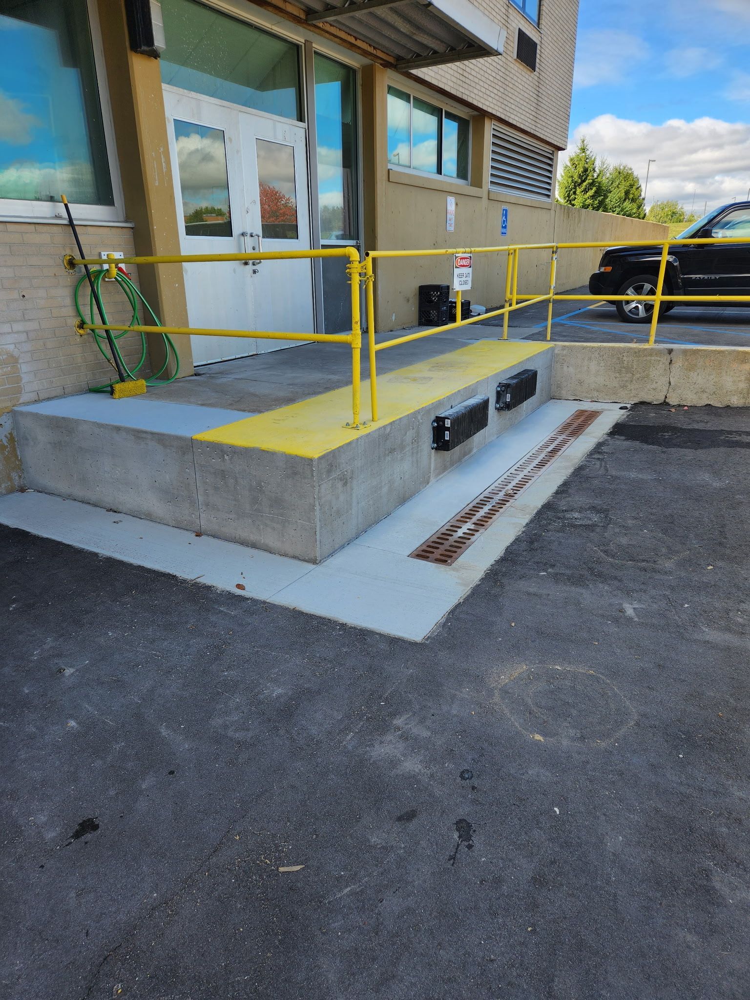 A car is parked in front of a building with a ramp and a yellow railing.