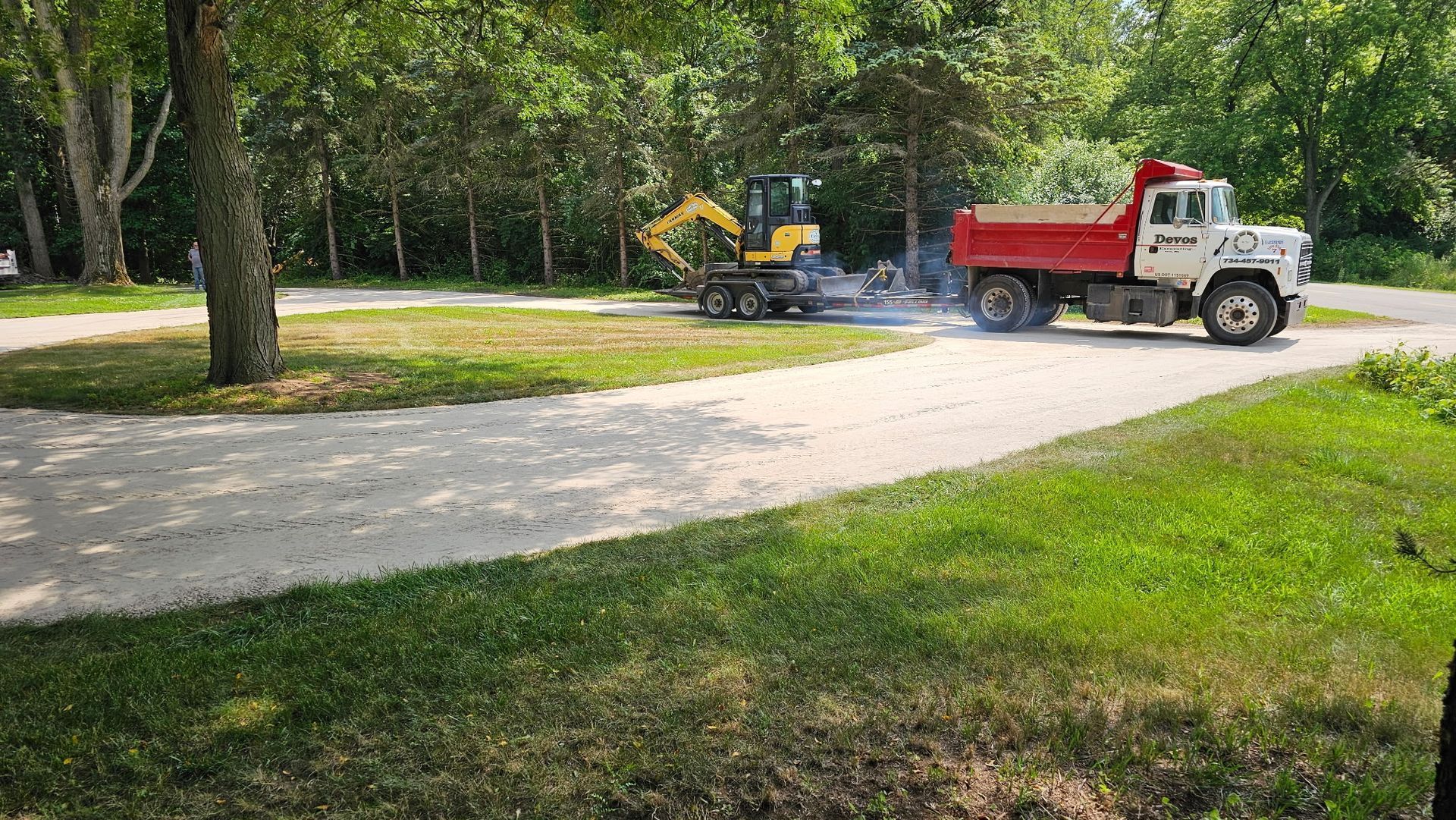 A red dump truck is driving down a dirt road next to a yellow excavator.