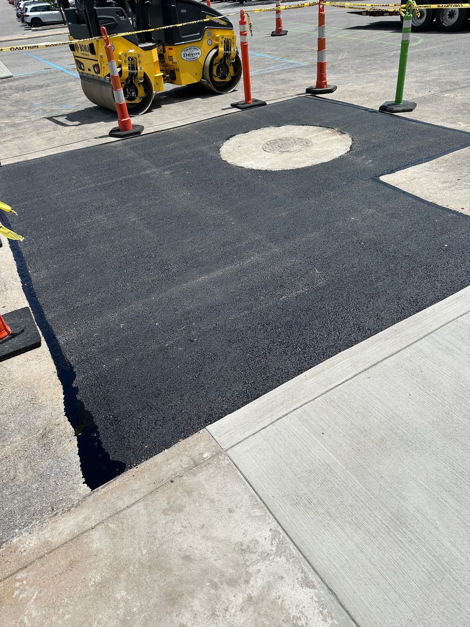 A yellow roller is laying asphalt in a parking lot.