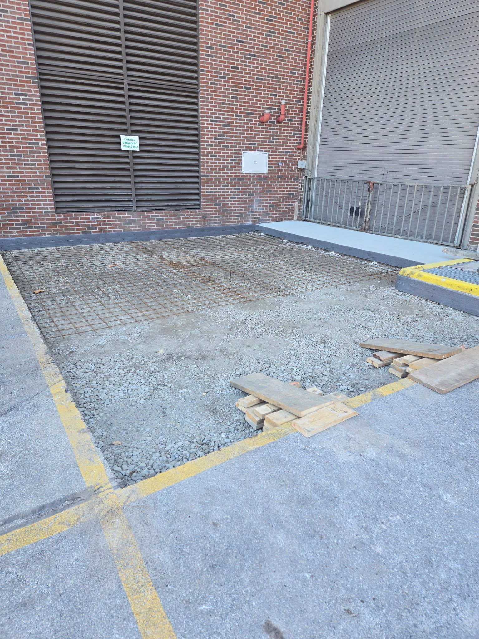 A gravel-filled loading dock with yellow painted edges and a brick wall in the background - before