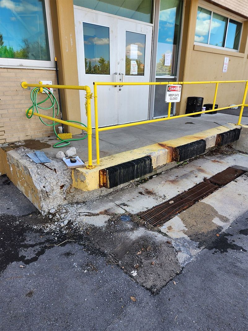 A yellow railing is surrounding a concrete ramp in front of a building.