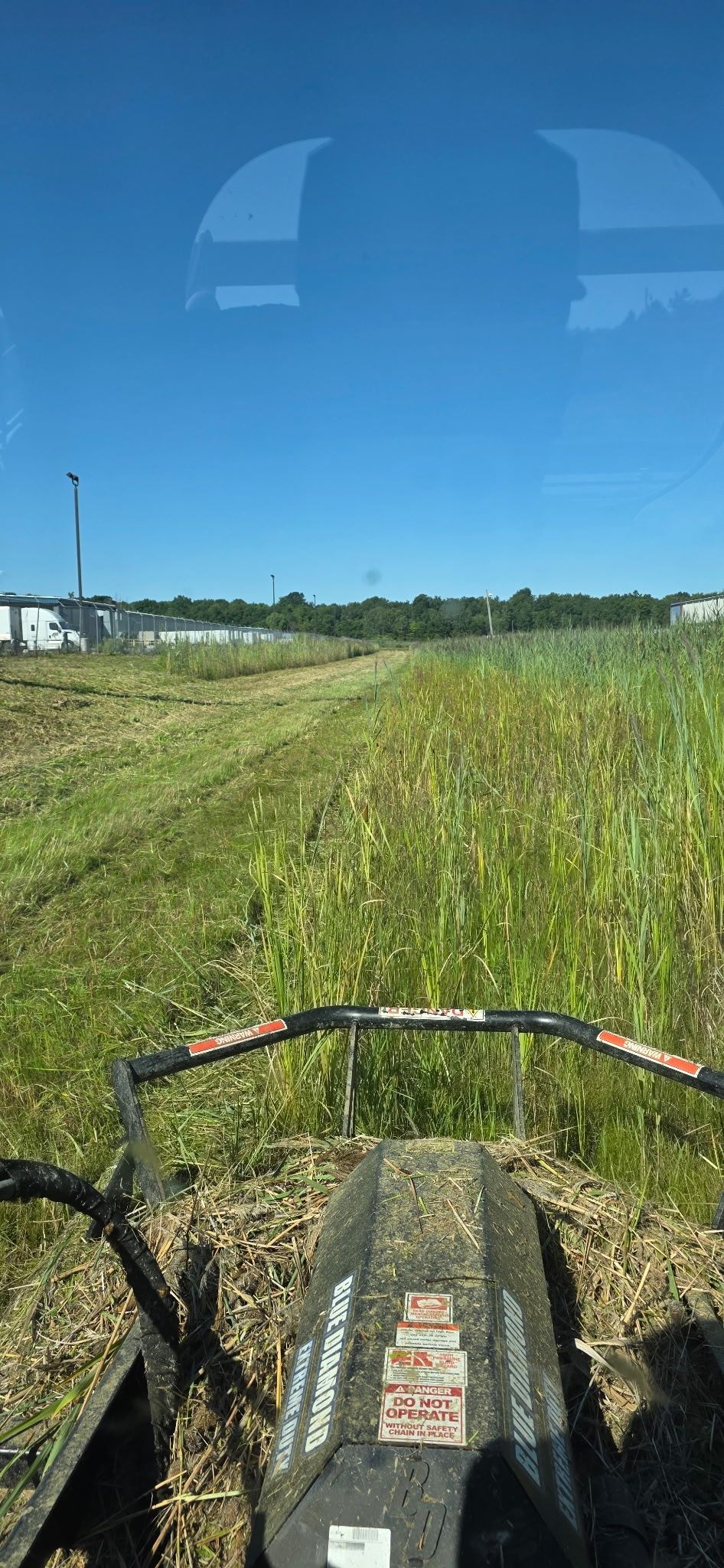 View from a mower driving through a green field under a clear blue sky