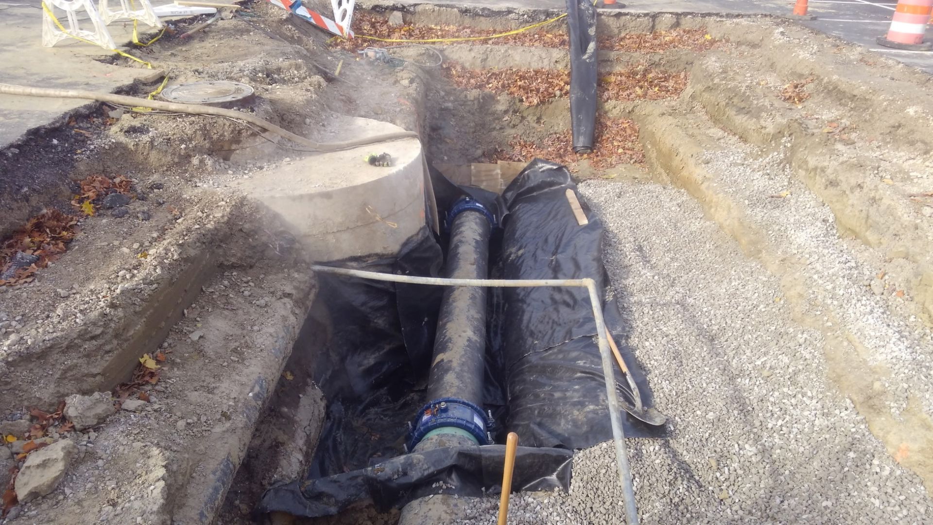Construction site with a pipe in a trench, surrounded by gravel and soil.