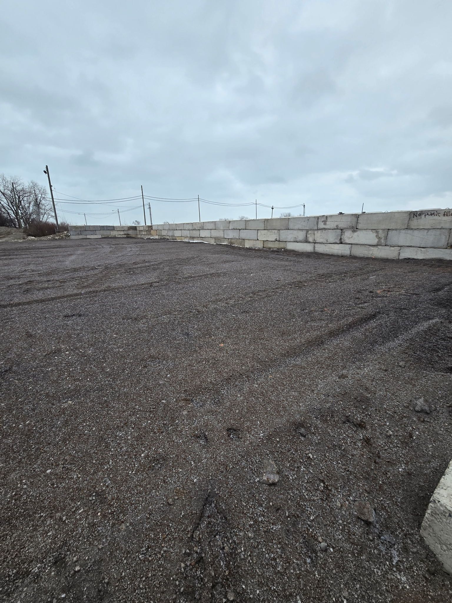 Gravel-covered lot next to a concrete block wall under a cloudy sky.
