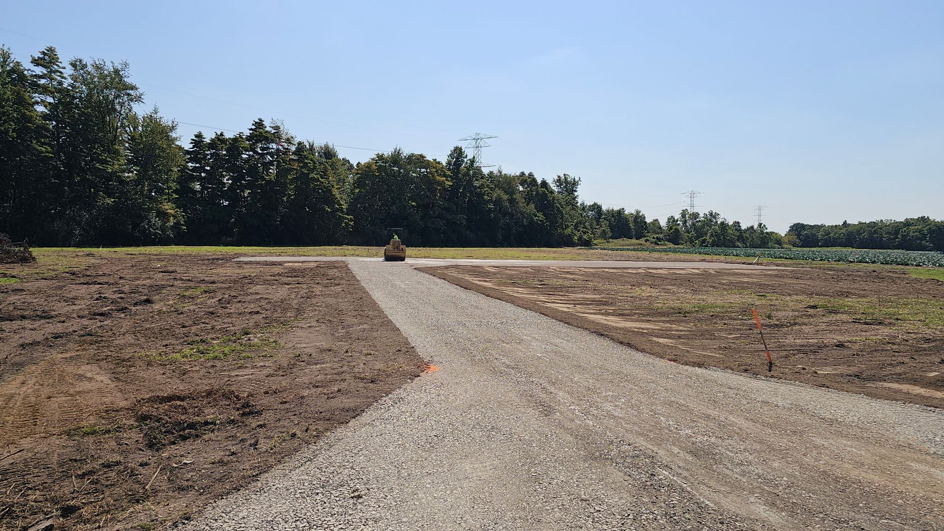 Gravel road leading through a cleared field toward treeline under a blue sky.