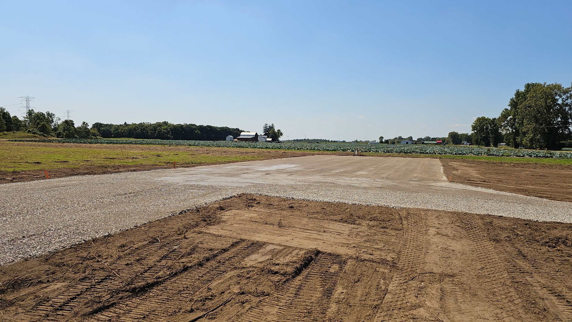 Gravel path intersections across a dirt field, with crops and trees visible under a blue sky.