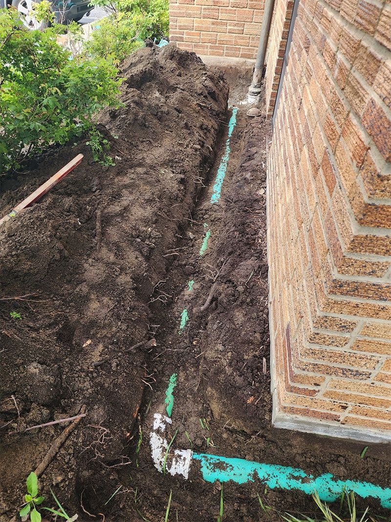 A green pipe is being installed in the dirt next to a brick wall.