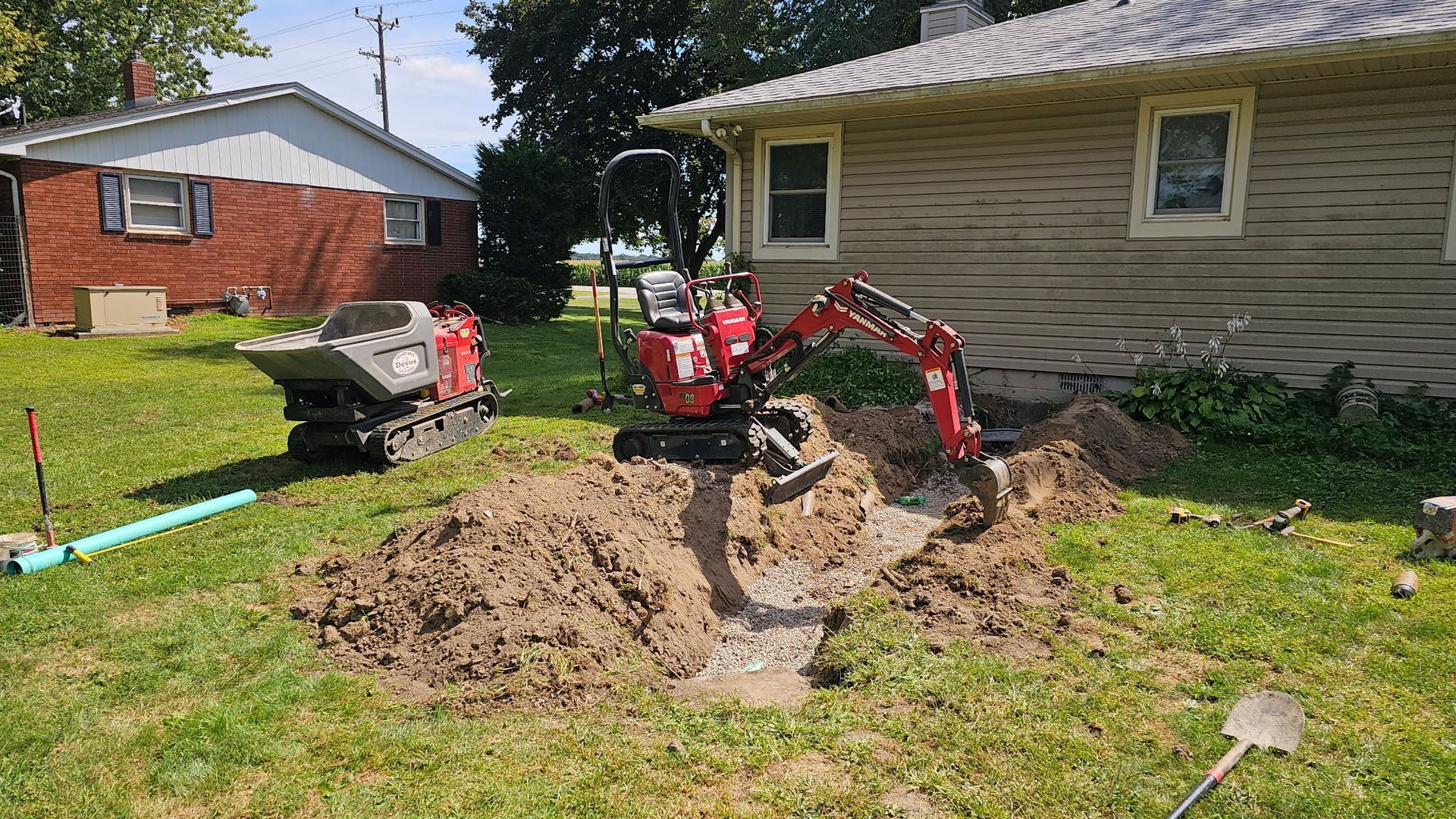 Mini excavator digging a trench in a yard with a small house in the background.