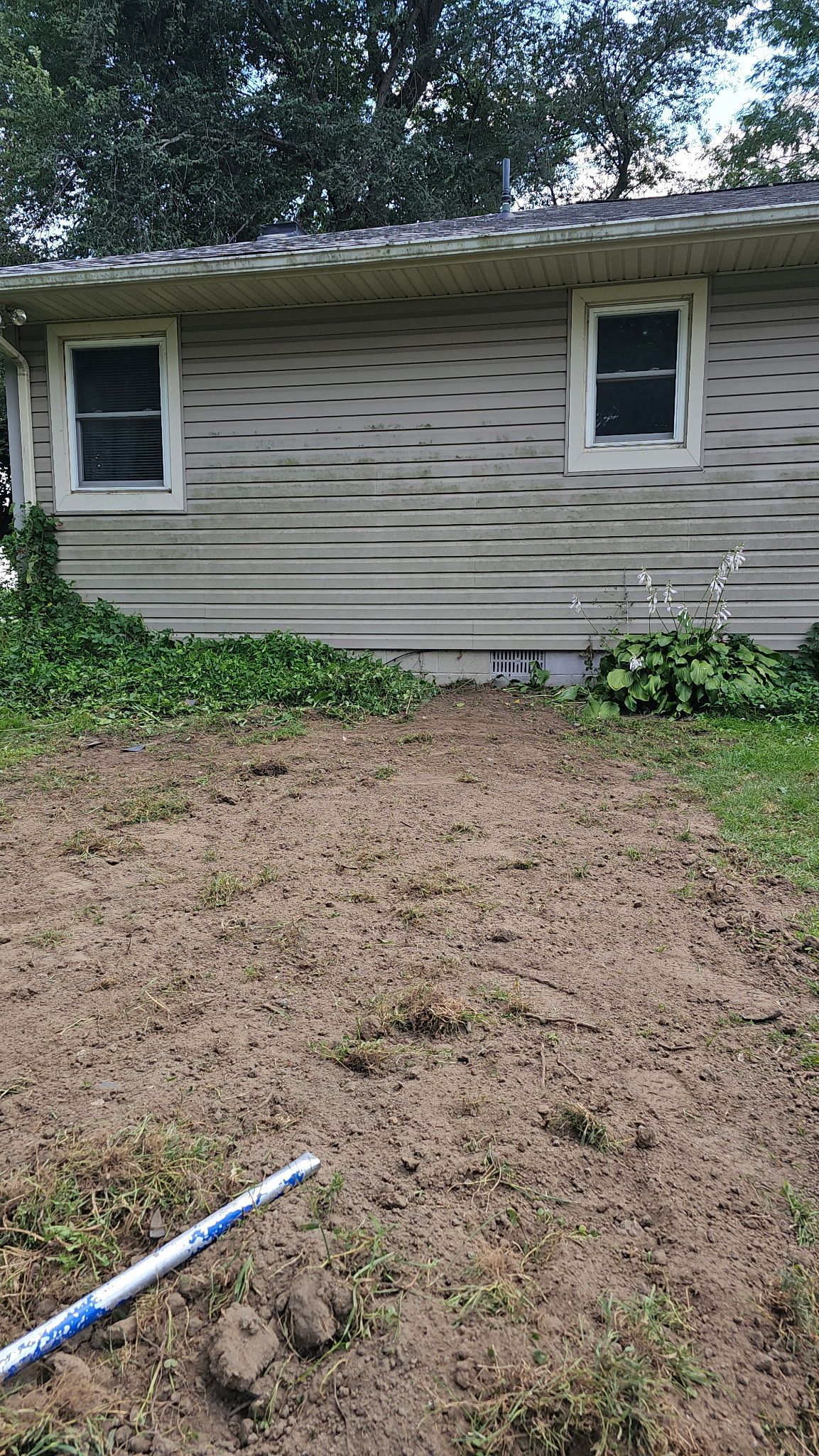 A dirt patch in front of an old building with two windows; a blue and white tool rests on the ground.