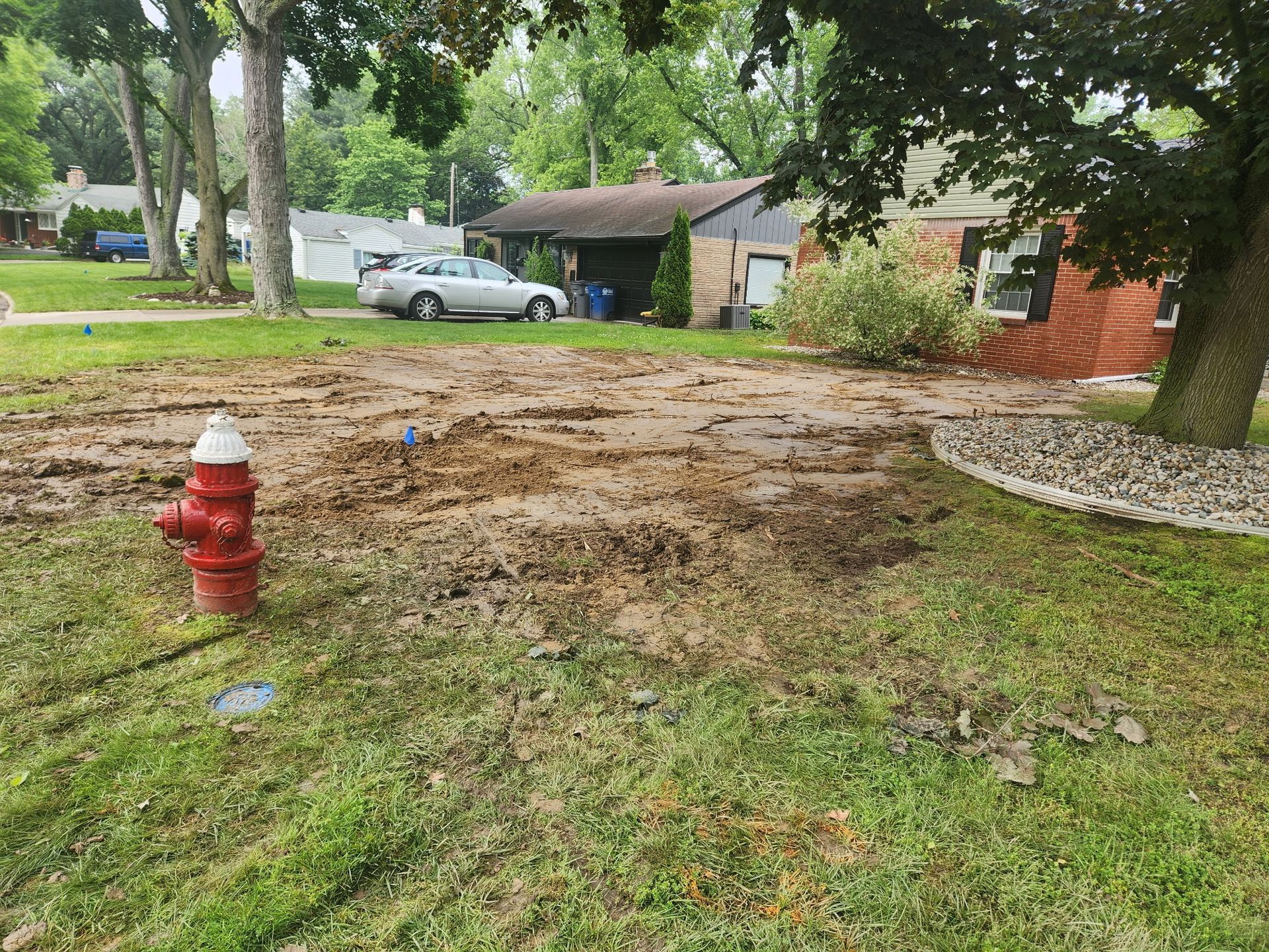 A red fire hydrant is in the middle of a muddy yard.