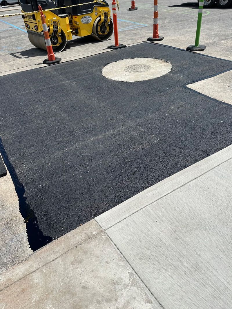 A yellow roller is rolling asphalt in a parking lot.