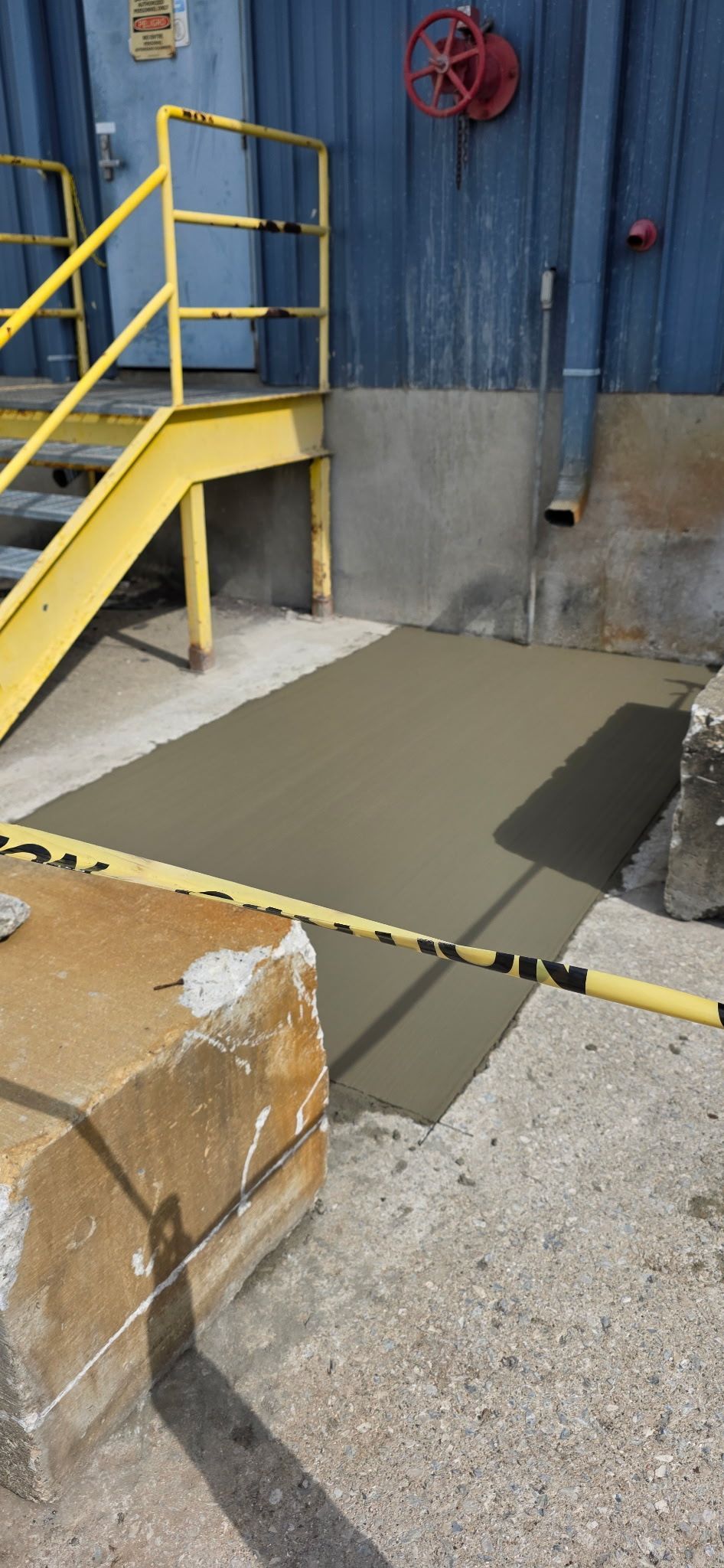 Industrial loading area with yellow stairs, blue wall, and a temporary concrete patch in the ground.