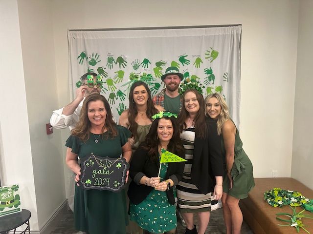 A group of people are posing for a picture in front of a green background.